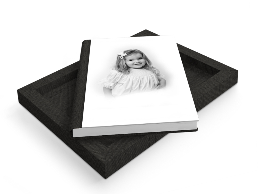 Black cloth-bound heirloom album displaying a black and white portrait of a young girl on its open white page